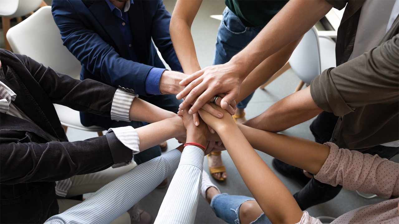 Diverse team members join hands in a group huddle.